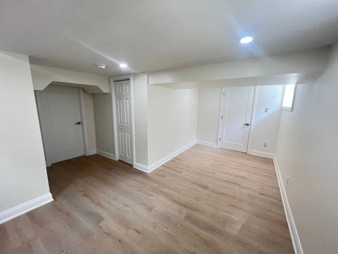 Finished basement with new wood-look flooring and fresh paint, door open at the back