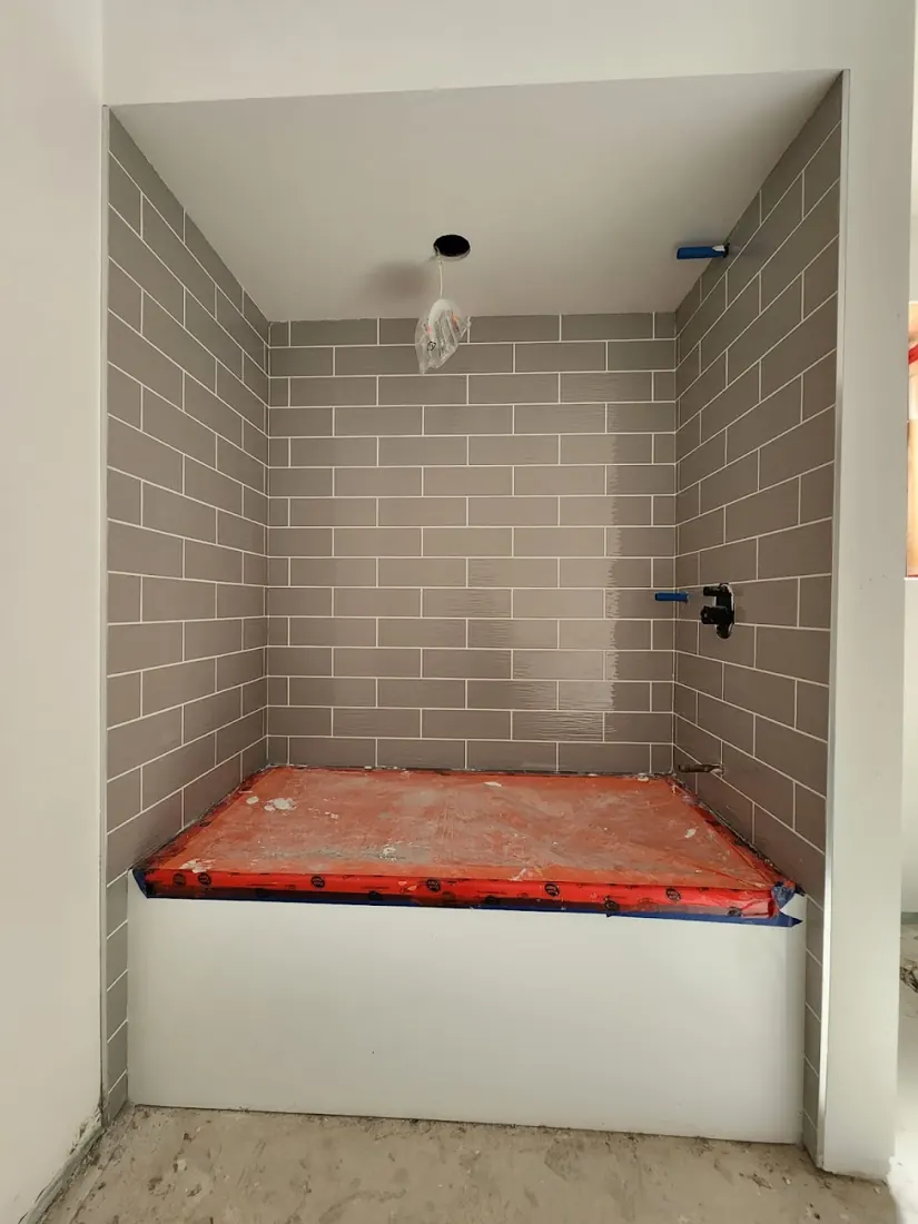Shower alcove with grey tile walls and a red waterproofing membrane on the base