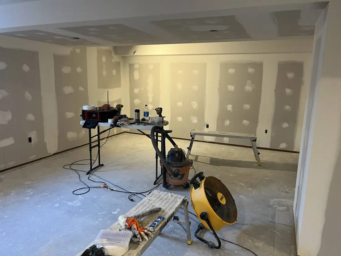 Basement mid-build with drywall taped and a fan on the floor